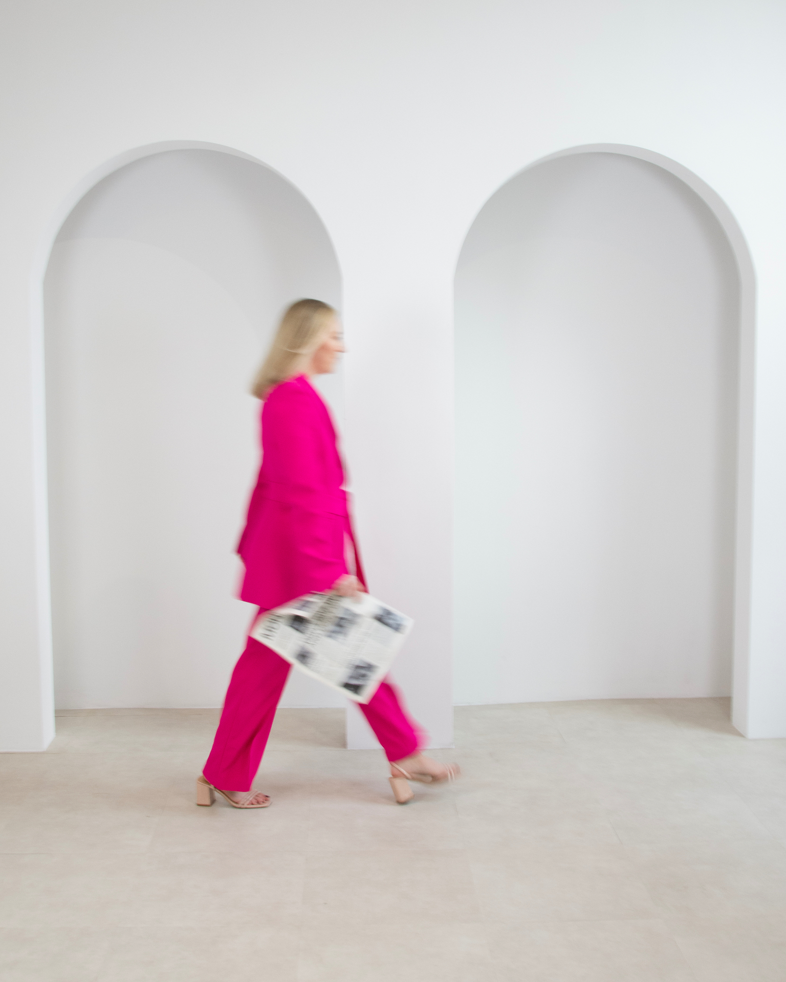 Founder in pink suit walking past arched wall